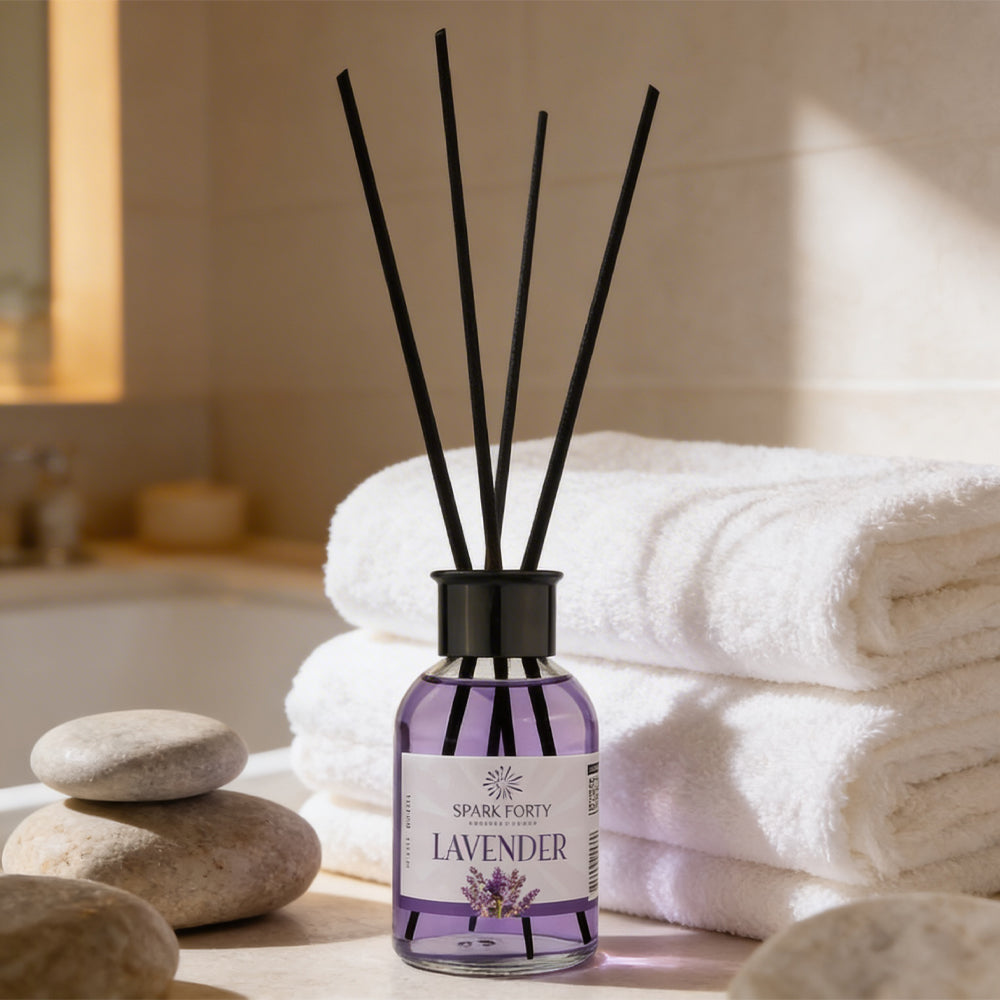 Sparkforty Lavender premium reed diffuser with black reeds in a purple glass bottle, displayed with folded towels and spa stones in a relaxing bathroom setting.