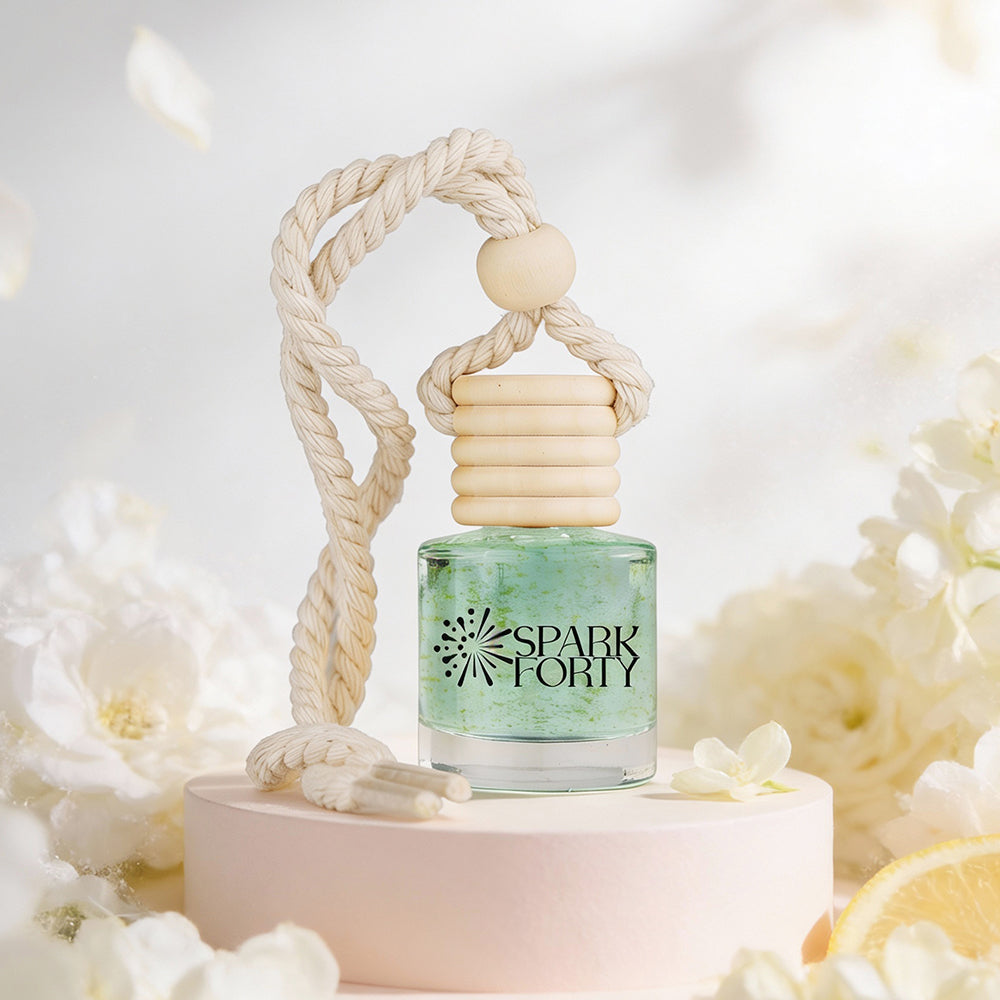 Sparkforty Jasmine car air freshener with a clear glass bottle, wooden diffuser cap, and cotton rope displayed on a pedestal surrounded by white jasmine flowers and citrus accents.