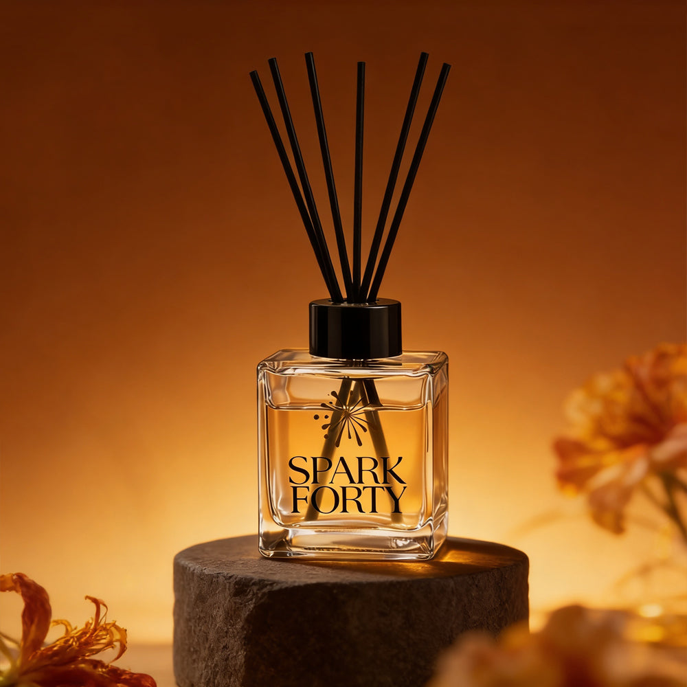 Sparkforty Rouge 540 reed diffuser in a clear glass bottle with black reeds displayed on a stone pedestal against a warm amber background. Luxury home fragrance diffuser inspired by amber, jasmine, saffron, and woody notes for long-lasting scent in living rooms, bedrooms, bathrooms, and offices.