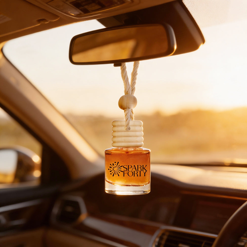 Sparkforty Sandal Amber car air freshener hanging from a vehicle rearview mirror, featuring a premium glass bottle with a wooden diffuser cap and cotton rope, illuminated by warm golden sunset light for a luxurious long-lasting car fragrance.